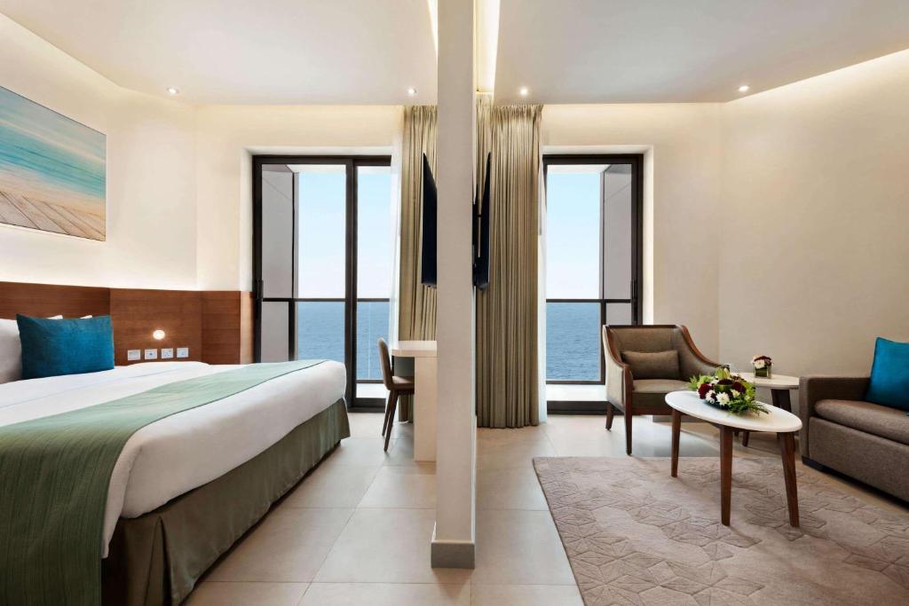 a hotel room with a bed and a couch and windows at Wyndham Garden Ajman Corniche in Ajman 