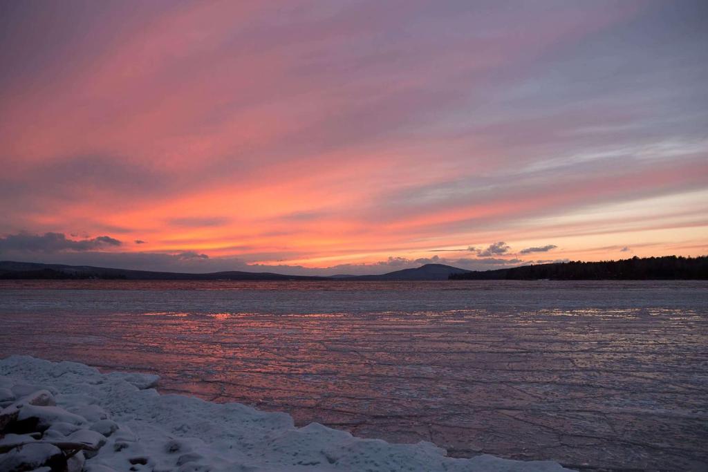 una puesta de sol sobre un cuerpo de agua con hielo en Rangeley Lake Resort a Ramada by Wyndham en Rangeley