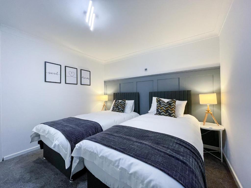 two beds in a bedroom with white walls and two lamps at Richmere Court in Wolverhampton