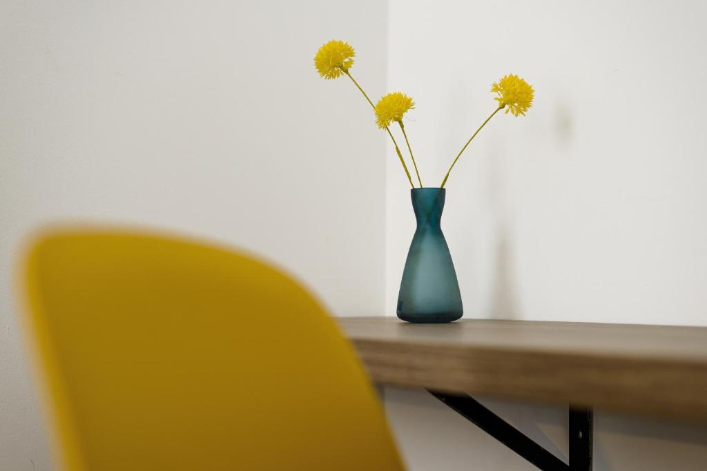 a blue vase with flowers on a table with a yellow chair at RES City Residence Hotel Budapest in Budapest