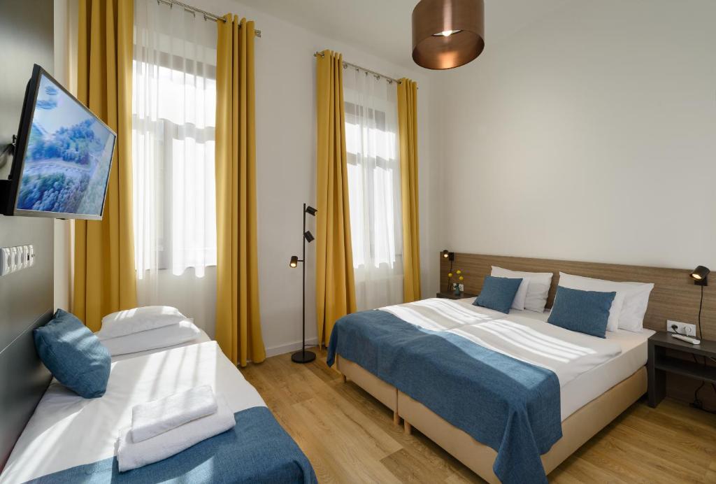 two beds in a hotel room with yellow curtains at RES City Residence Hotel Budapest in Budapest