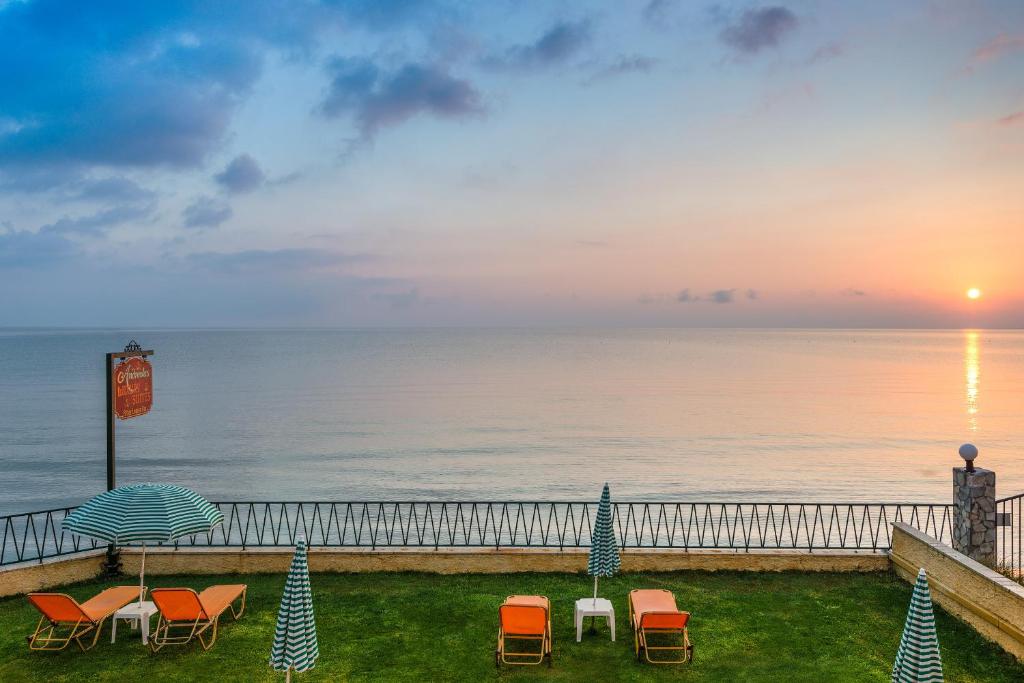 チィリヴィにあるアンドレオラス ラグジュアリー スイーツのビーチの夕日の景色を望む客室で、椅子とパラソルが備わります。