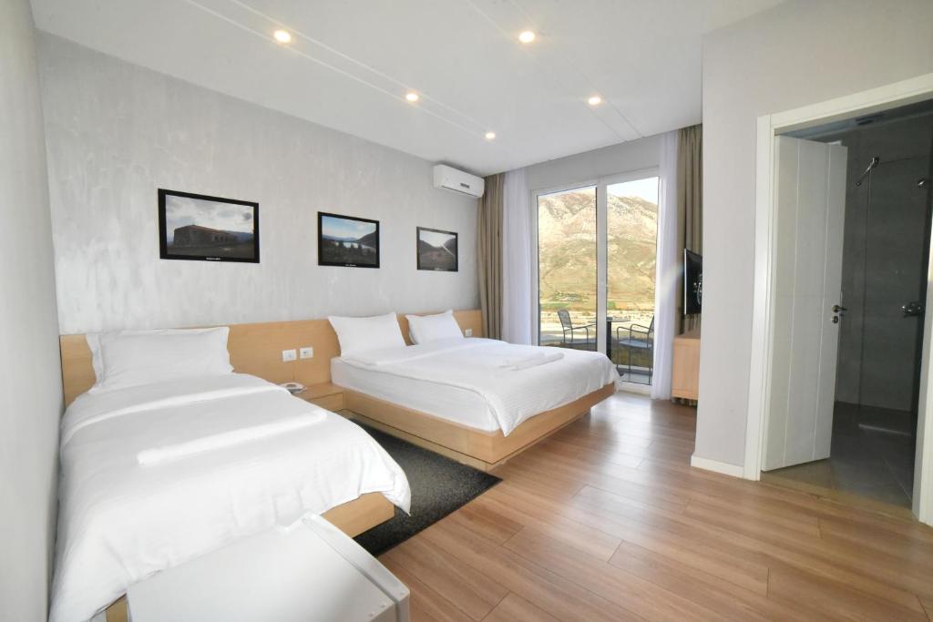 een slaapkamer met 2 bedden en een groot raam bij Hotel Auto Grill Roberti in Tepelenë