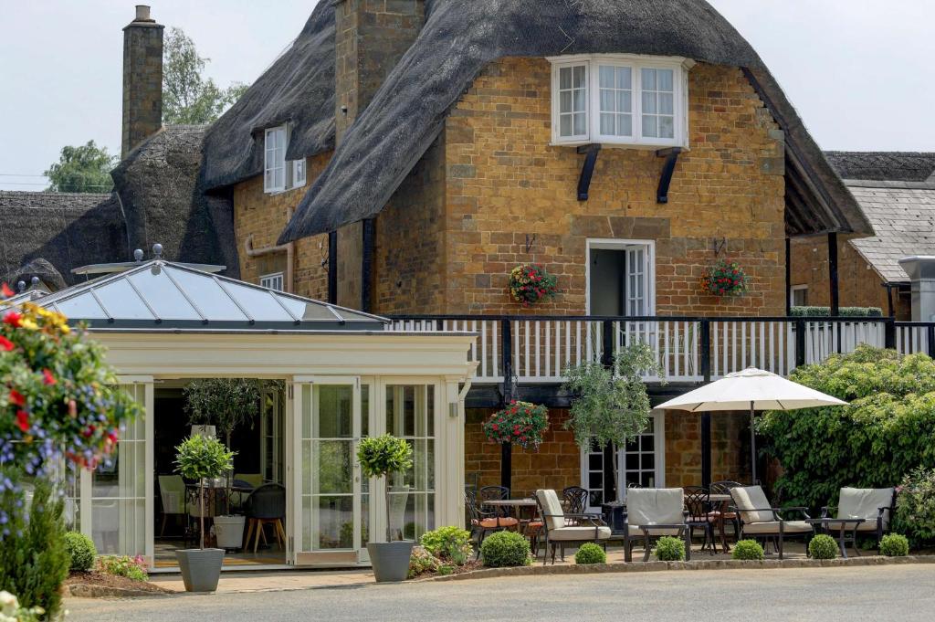 a thatched house with chairs and an umbrella at Banbury Wroxton House Hotel in Banbury