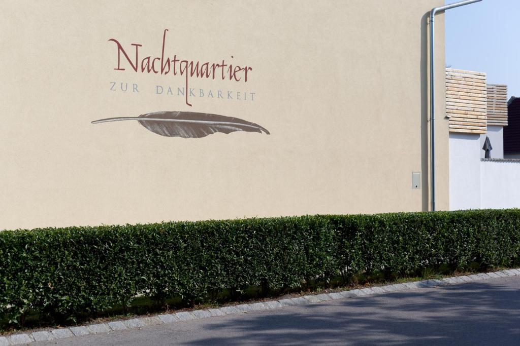 a sign on the side of a building with a hedge at Nachtquartier Zur Dankbarkeit in Podersdorf am See