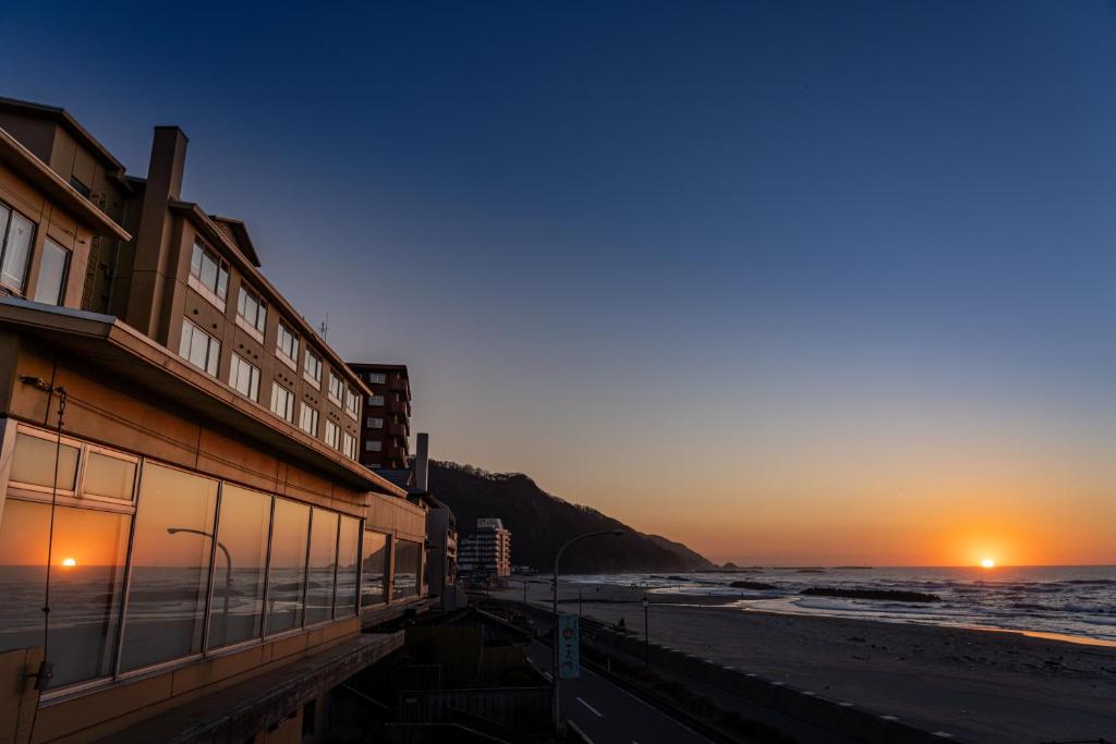 a building on the beach with the sunset in the background at Ikkyu -Seaside Hotel- in Tsuruoka