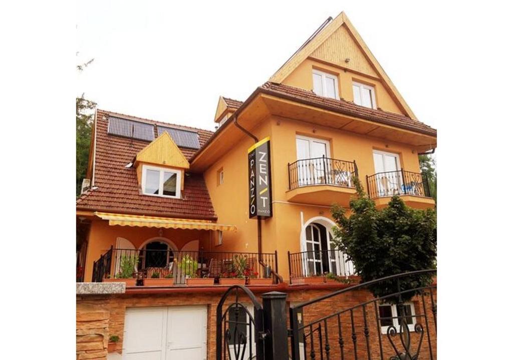 a yellow house with a fence in front of it at Zenit Panzió in Miskolctapolca