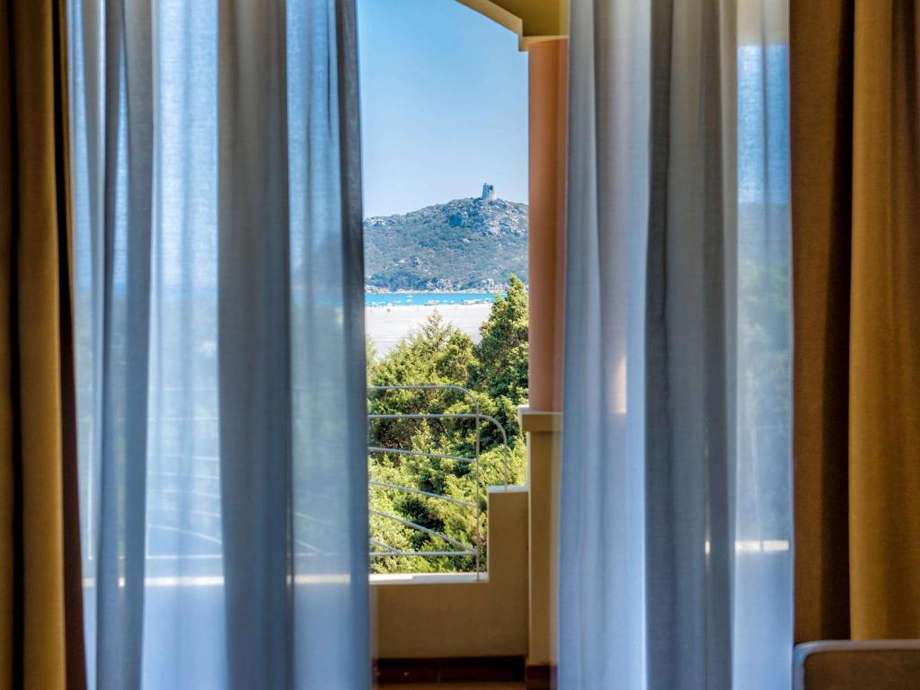 a window with a view of a beach from a hotel room at Almar Timi Ama Resort & Spa in Villasimius