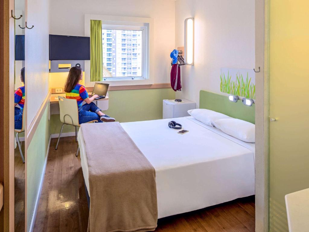 a bedroom with a bed and two people sitting at a desk at ibis budget Belo Horizonte Minascentro in Belo Horizonte