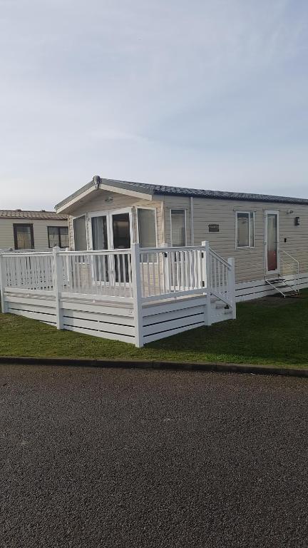 a white house with a porch and a white fence at RICK'S RETREAT static caravan near the beach with free wifi in Lossiemouth
