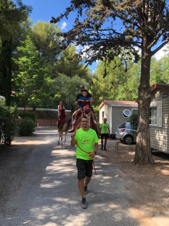 Um homem a correr por uma estrada com uma pessoa a montar um camelo. em Camping Marina Plage em Vitrolles