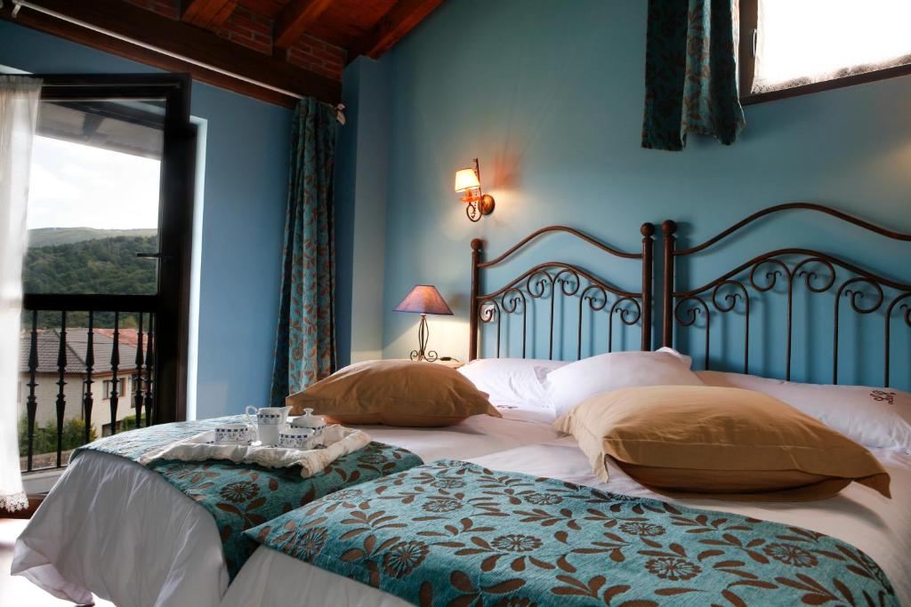two beds in a bedroom with blue walls and a window at La Riguera de Ginio in Ucieda de Arriba