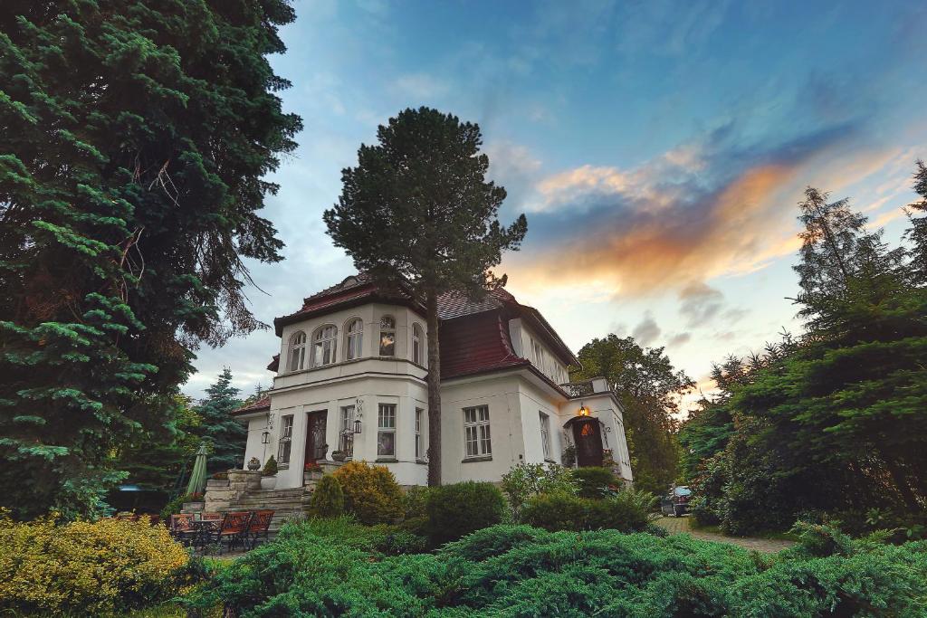 une grande maison blanche avec un arbre au-dessus dans l'établissement Dworek Genny, à Polanica-Zdrój