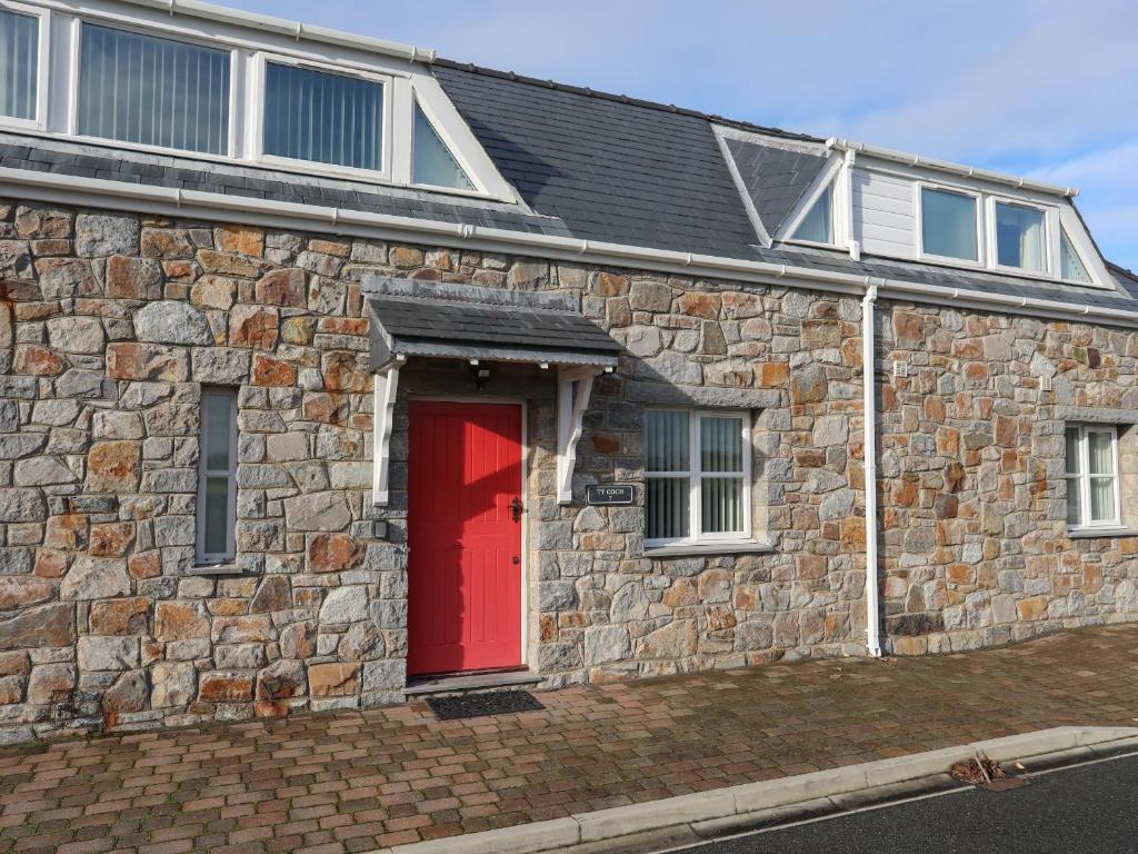 a brick house with a red door on a street at Tyn Towyn - Ty Coch in Trearddur