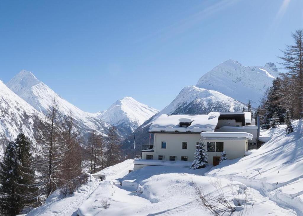 a house in the snow with mountains in the background at Waldhotel Fletschhorn Saas-Fee in Saas-Fee