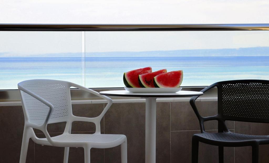 a table with a plate of watermelon and two chairs at Ostria Sea Side Hotel in Hanioti