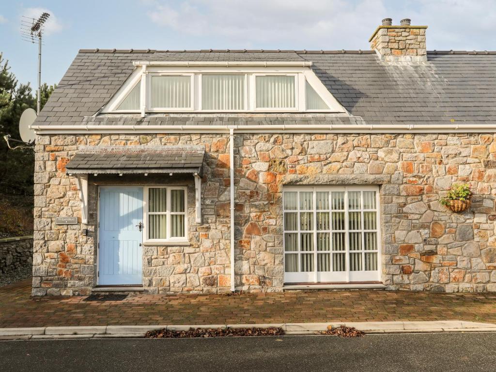 a stone house with a blue door and two windows at Tyn Towyn - Ty Glas Golau in Trearddur