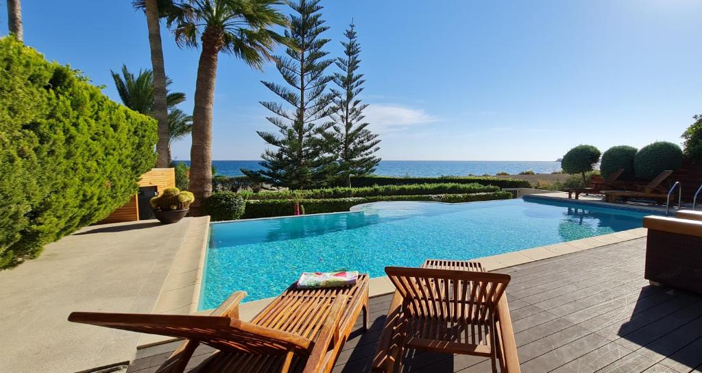 a swimming pool with two chairs and the ocean at Villa del Mar in Mazotos