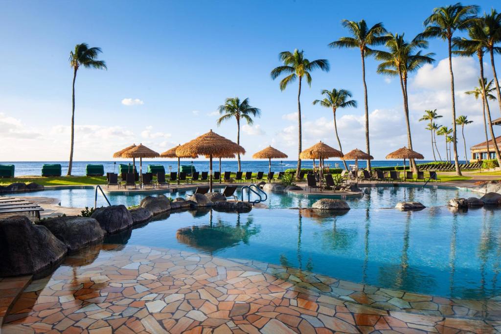 a resort swimming pool with palm trees and the ocean at Sheraton Kauai Resort in Koloa