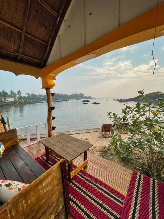 a wooden deck with a table and a view of the water at La Rocha in Patnem