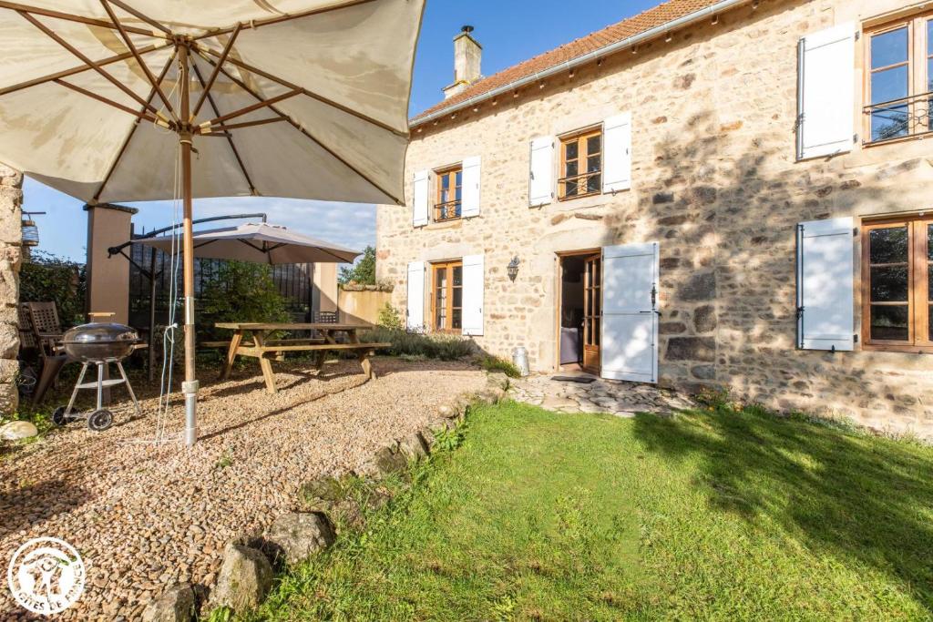 ein Haus mit einem Regenschirm, einem Tisch und einem Grill in der Unterkunft Aux 2 Puys - Gîte "Le Lemptégy" in Saint-Priest-des-Champs