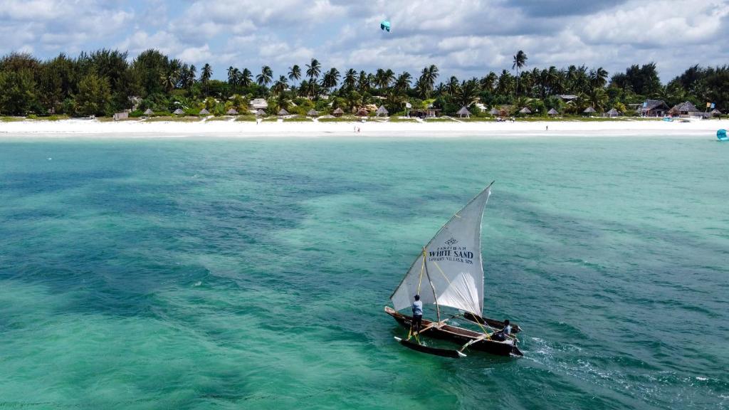 a small sail boat in the water with a beach at Zanzibar White Sand Luxury Villas & Spa - Relais & Chateaux in Paje