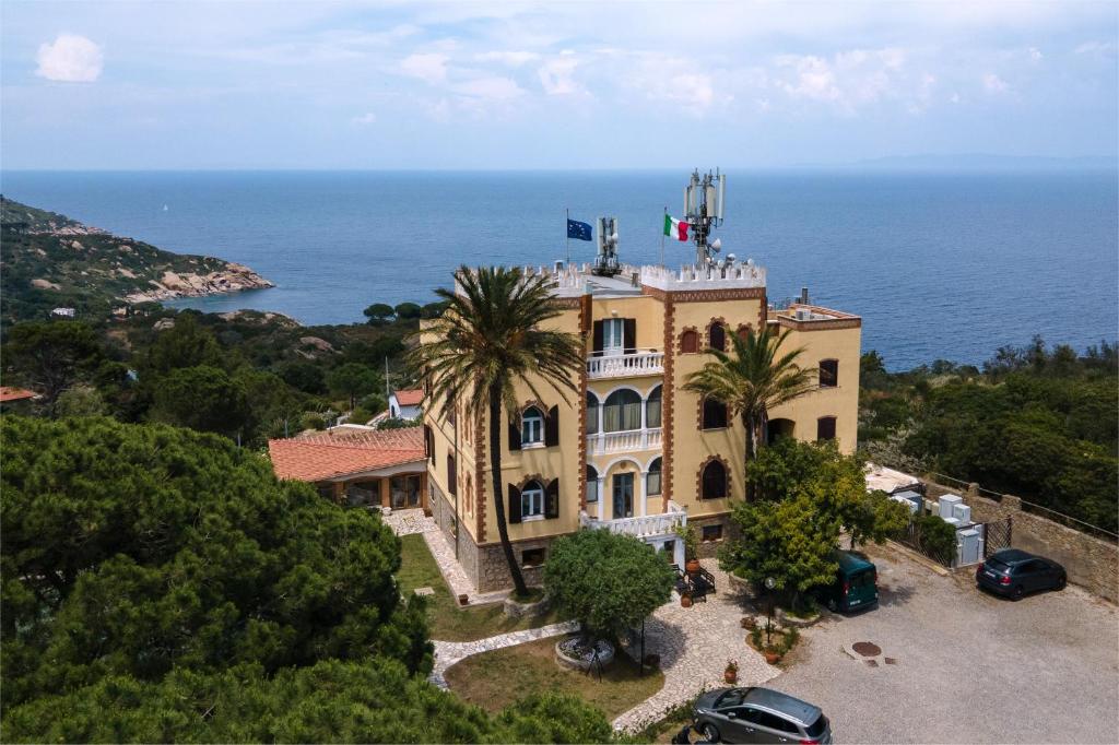 a building with palm trees in front of the ocean at Hotel Castello Monticello in Giglio Porto