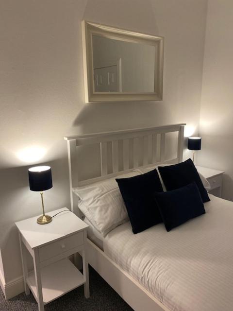 a white bed with black pillows and a table with a lamp at Glenfinnan - Two Bedroom Apartment in Fife