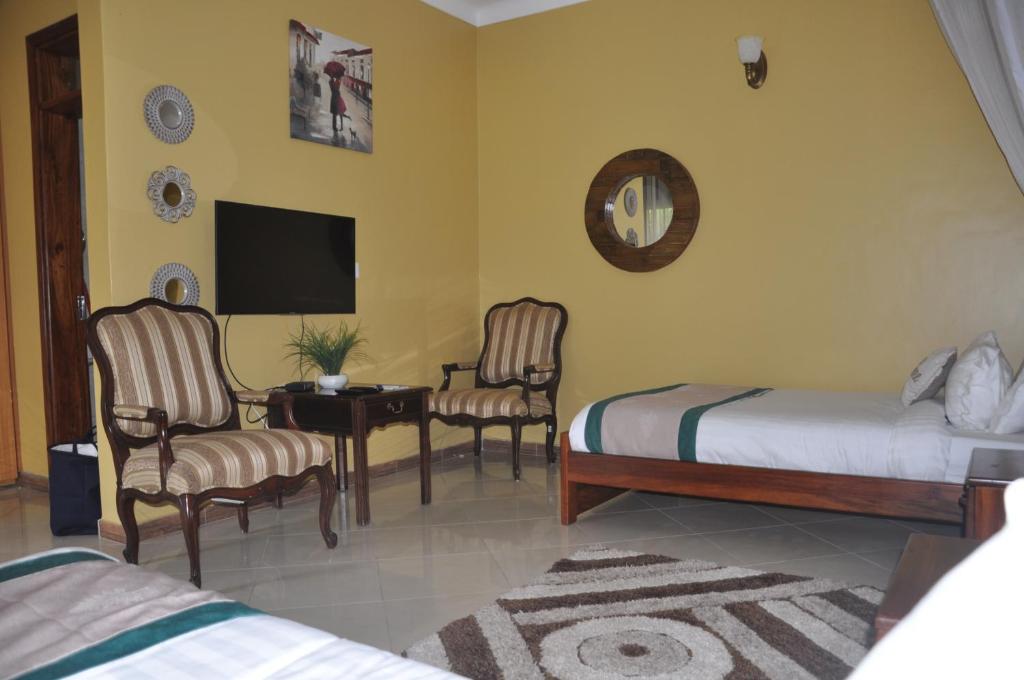 a bedroom with two beds and a tv and chairs at Home Bliss Hotel- Fort portal Uganda in Fort Portal
