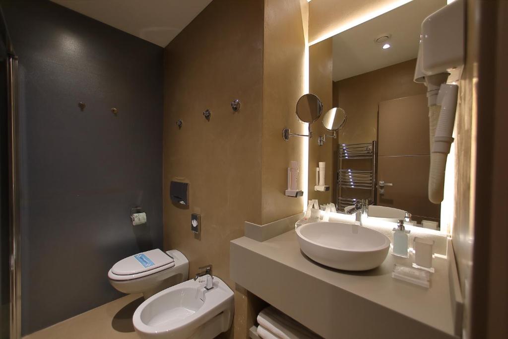 a bathroom with two sinks and a toilet and a mirror at Hotel Bell'arrivo by Dori in Peschiera del Garda