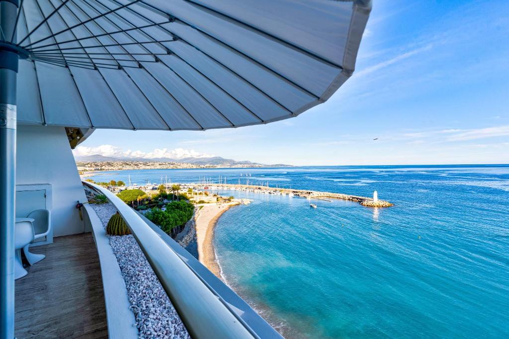 uma vista para a praia a partir de uma varanda com um guarda-sol em Annabelle em Villeneuve-Loubet