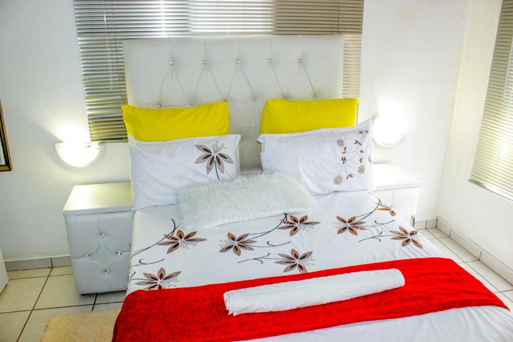 uma cama branca com um cobertor vermelho e almofadas em Motseleng Guest House em Palapye