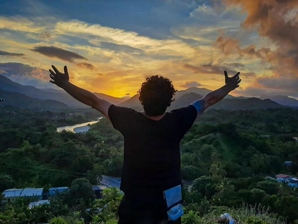 a man standing on top of a hill with his arms outstretched at Cristal Tayrona in Los Naranjos