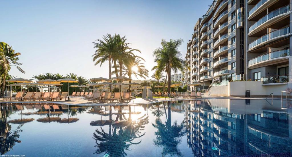 a swimming pool with chairs and palm trees and a building at Radisson Blu Resort Gran Canaria in La Playa de Arguineguín