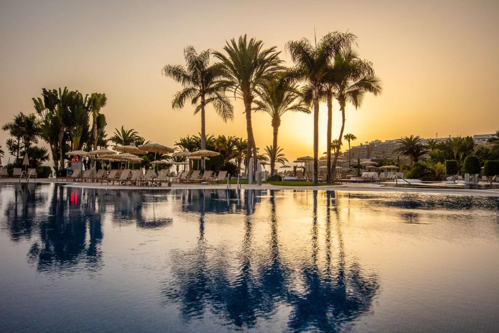 a swimming pool with palm trees and a sunset at Radisson Blu Resort Gran Canaria in La Playa de Arguineguín