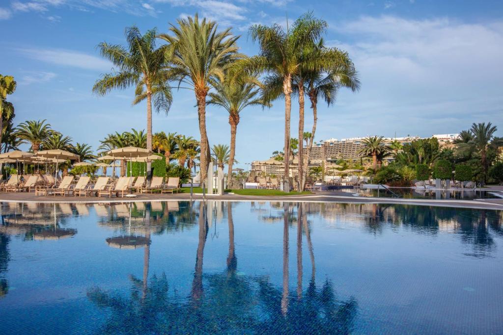 a large swimming pool with palm trees and chairs at Radisson Blu Resort Gran Canaria in La Playa de Arguineguín