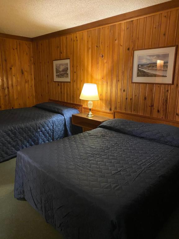 two beds in a room with wooden walls and a lamp at Glacier View Inn in Haines Junction