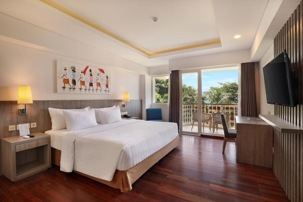 a bedroom with a large white bed and a balcony at ASTON Canggu Beach Resort in Canggu