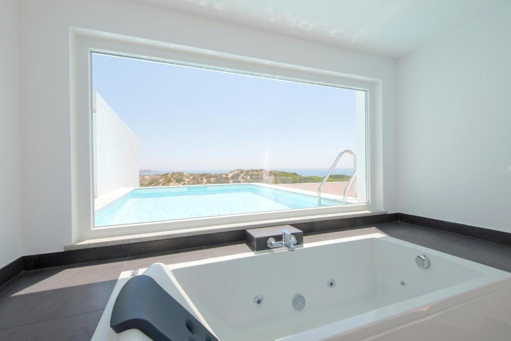 a bath tub in a room with a large window at Penthouse with rooftop pool - Duna Parque Group in Vila Nova de Milfontes