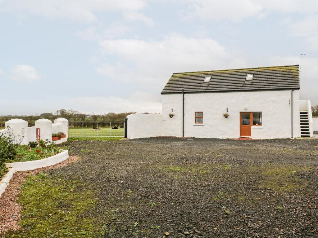 a white house with a red door and a yard at May's Cottage in Bushmills