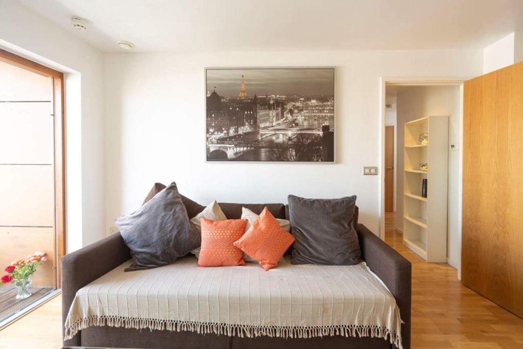 a living room with a couch with orange and gray pillows at Room with private bathroom in a modern two bedroom two bathroom flat in London