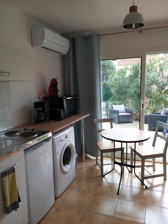 eine Küche mit einer Waschmaschine und einem Tisch mit Stühlen in der Unterkunft Rez de jardin cosy avec terrasse fleurie in Arles-sur-Tech
