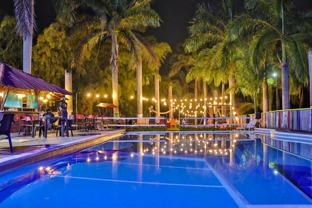 a swimming pool with lights and palm trees at night at Palmas De Santa Elena in Quimbaya