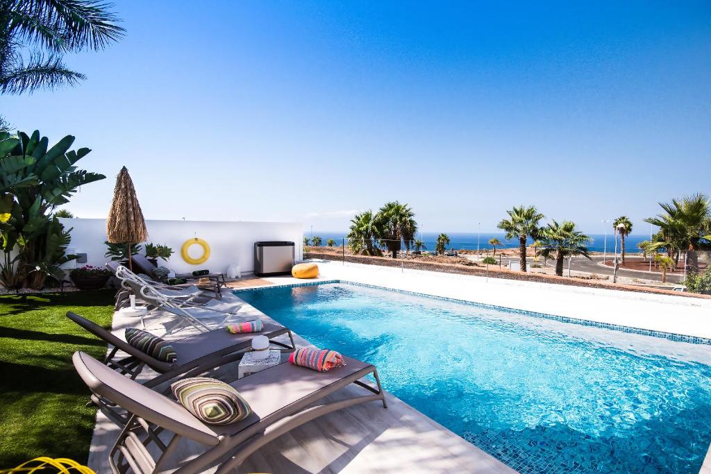 a swimming pool with chaise lounge chairs and the ocean at Villa Caleta Golf in Adeje