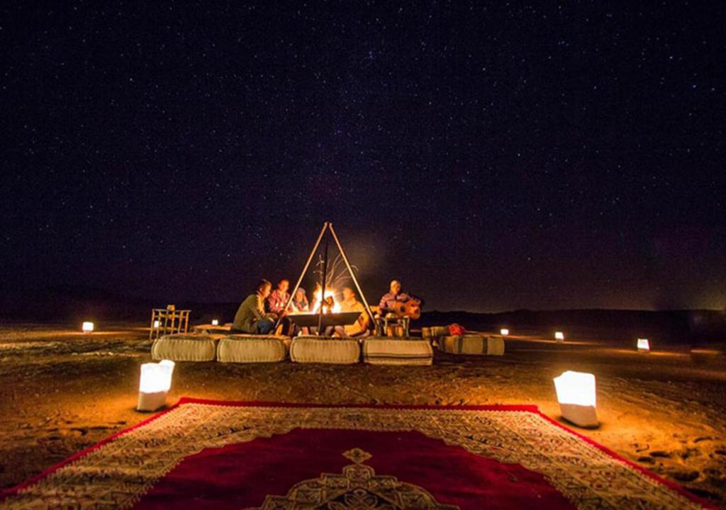 Un groupe de gens assis autour d'un feu la nuit dans l'établissement Sahara Relax Camps, à Zagora