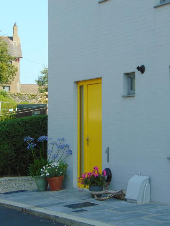 a yellow door on a white house with flowers at Driftwood, Donaghadee in Donaghadee