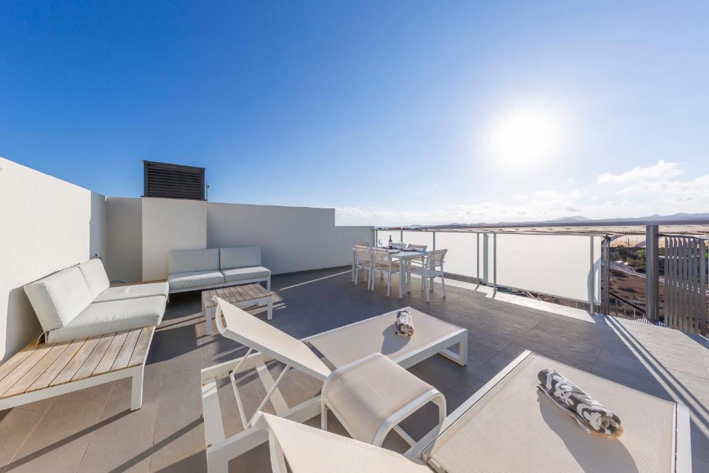 Elle comprend un balcon doté d'un mobilier blanc et offrant une vue sur l'océan. dans l'établissement MEDANO4YOU The Casa Celou Penthouse, à La Tejita