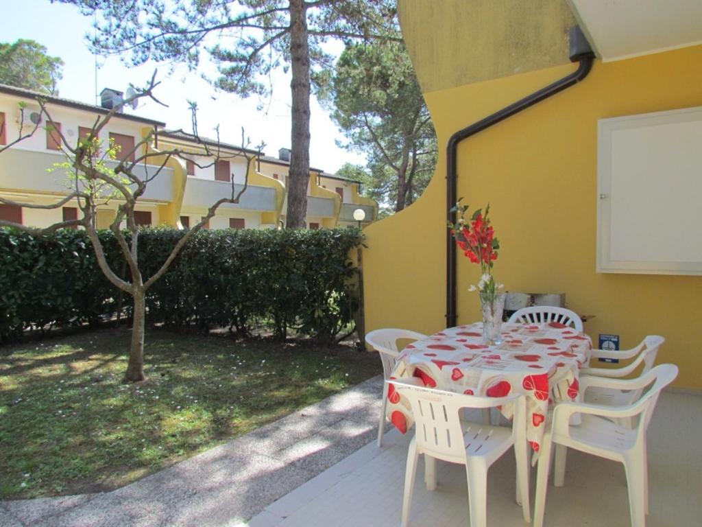 uma mesa com cadeiras brancas e uma toalha de mesa vermelha e branca em Lovely flat with garden and pool - Beahost em Bibione