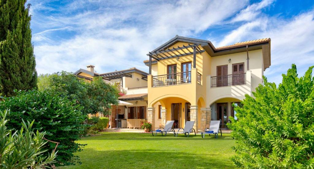 a large yellow house with chairs on the lawn at Ground floor apartment with golf and sea views - Roudias, Aphrodite Hills Resort in Kouklia