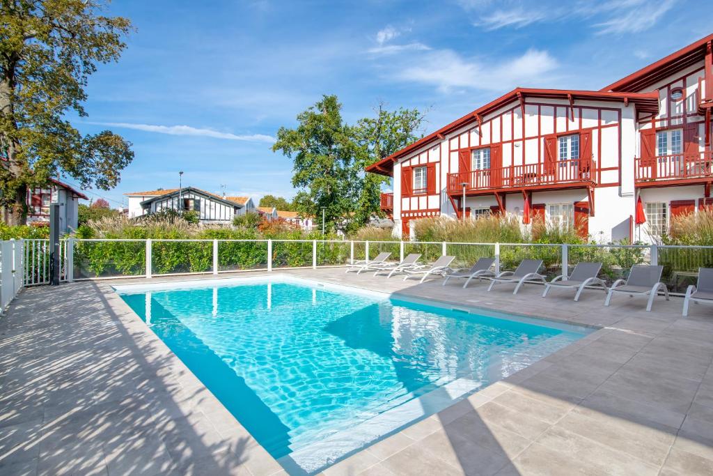 a swimming pool with chairs next to a building at Résidence Ker Enia Meublés de Tourisme in Cambo-les-Bains